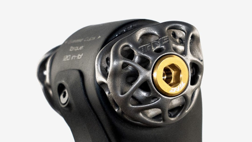 Black titanium bike component with gold hex bolt, TiNE TECH branding