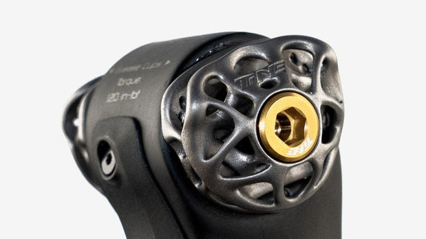 Black titanium bike component with gold hex bolt, TiNE TECH branding