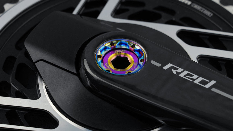 TiNE titanium crank cap with rainbow anodized finish on black crankset
