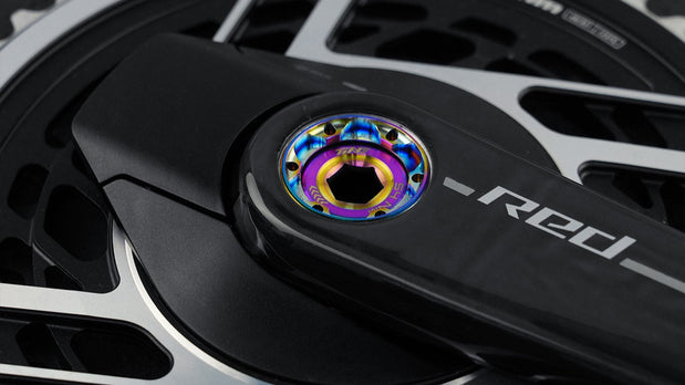TiNE titanium crank cap with rainbow anodized finish on black crankset