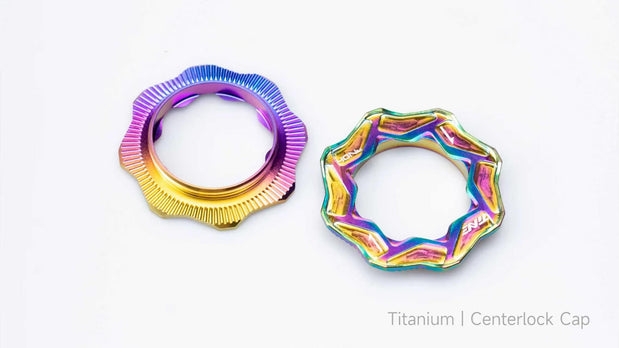 Two TiNE titanium centerlock caps in rainbow anodized finishes