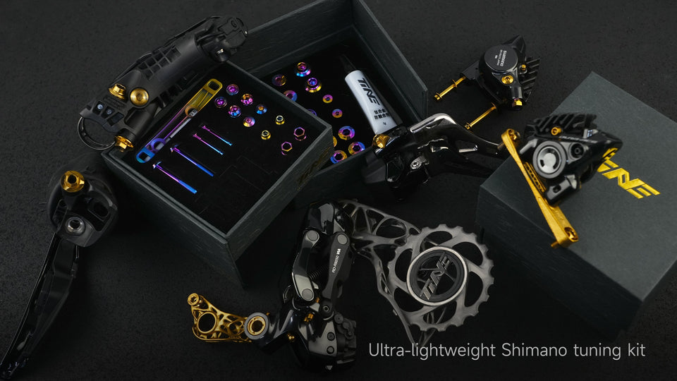 TiNE titanium bolt kit for Shimano 105 with rainbow anodized bolts, gold derailleur hardware, and chainring on black display case.