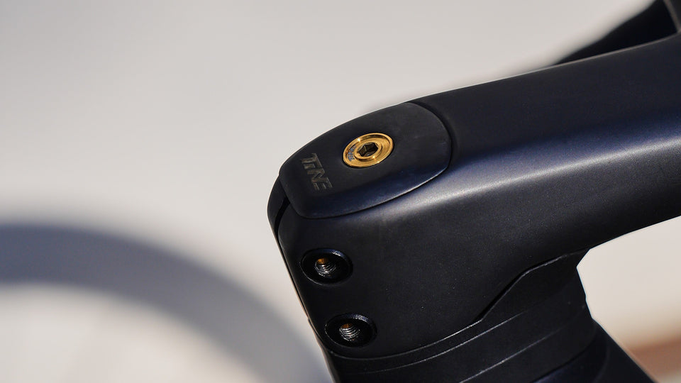 Black TiNE bicycle stem with gold titanium bolt heads and smooth matte finish, TiNE branding visible