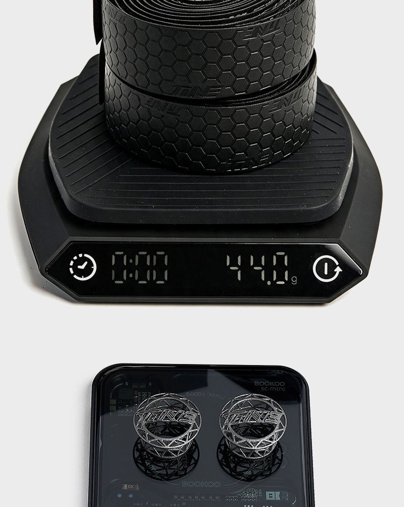 Black honeycomb handlebar tape weighing 44.0g on digital scale with two titanium bar ends displayed below